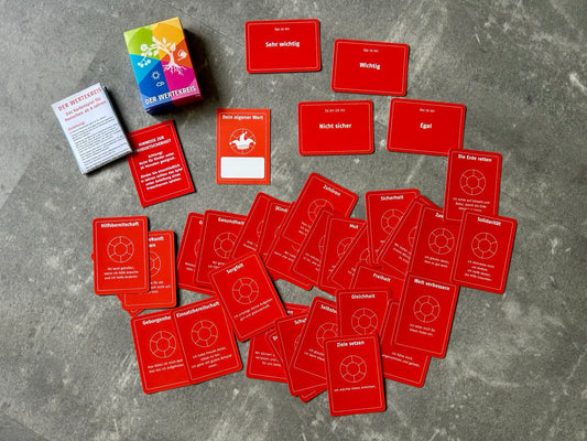 Das Bild zeigt das Wertekartenspiel „Der Wertekreis“ mit roten Wertekarten, Gruppenkarten wie „Egal“ und der bunten Spielbox auf grauem Untergrund.