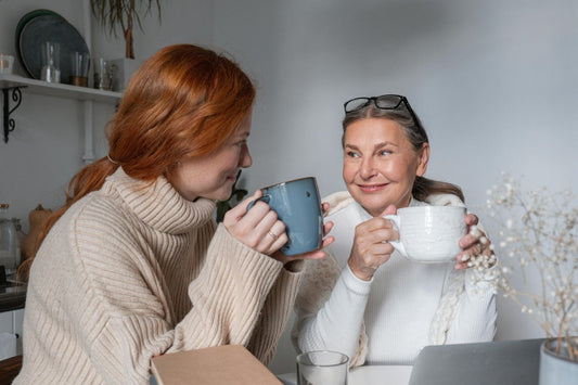 Zwei Frauen sitzen einander zugewandt und schauen sich freundlich an. Beide haben jeweils eine Tasse in der Hand.