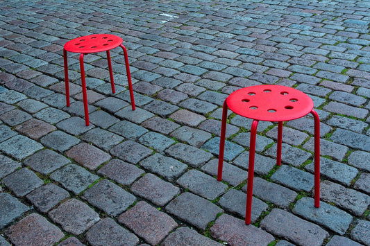 Zwei rote Metallhocker stehen auf Kopfsteinpflaster
