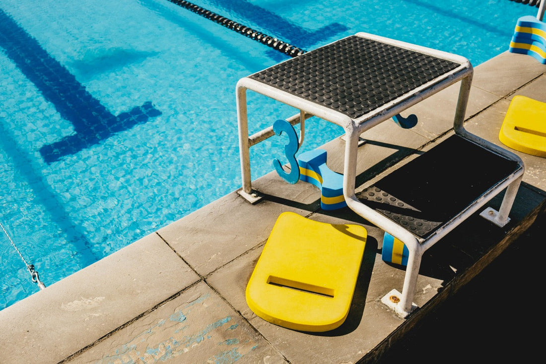 Ein Startblock am Schwimmbecken, daneben bunte Schwimmbretter
