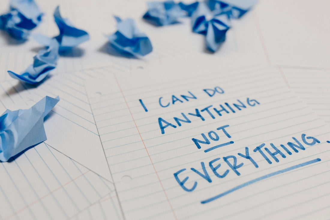 Ein handgeschriebener Zettel mit dem Satz „I can do anything – not everything“ liegt zwischen zerknüllten blauen Papierkugeln auf linierten Blättern.