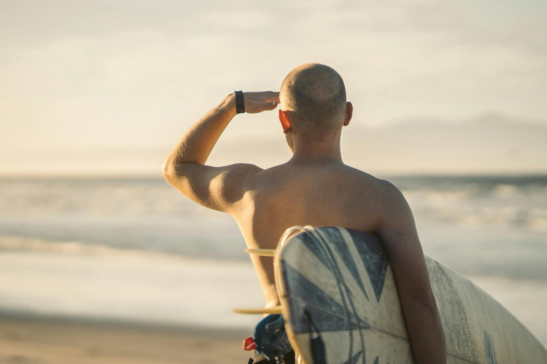 Ein Surfer steht am Strand, blickt neugierig in die Ferne und hält die Hand über die Augen