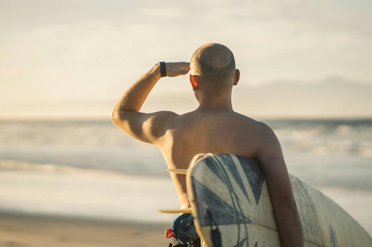 Ein Surfer steht am Strand, blickt neugierig in die Ferne und hält die Hand über die Augen