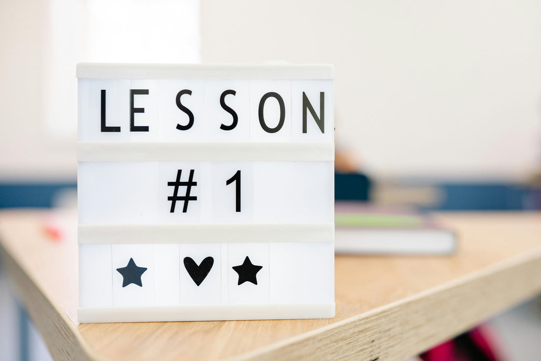 Weiße Leuchtbox mit der Aufschrift „Lesson #1“, darunter Herz und Sterne – sie steht auf einem Holztisch in einem hellen Raum, Symbol für Lernen und Neubeginn.