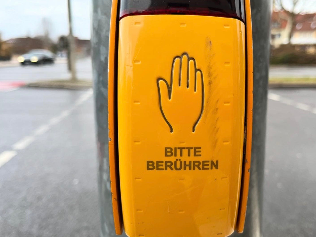 Nahaufnahme eines gelben Ampelknopfs mit der Aufschrift „Bitte berühren“. Der Hintergrund ist leicht verschwommen. Der Satz steht sinnbildlich für die menschliche Sehnsucht nach Verbindung und innerer Berührung.
