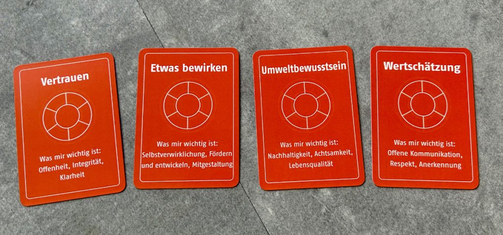 Vier orangefarbene Spielkarten des Werte-Kartenspiels aus der 1. Edition liegen nebeneinander.